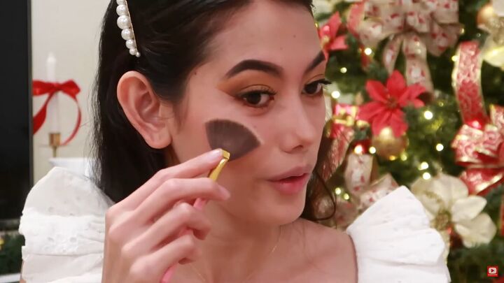 need some festive makeup inspo try this easy holiday makeup look, Applying highlighter to the tops of cheeks