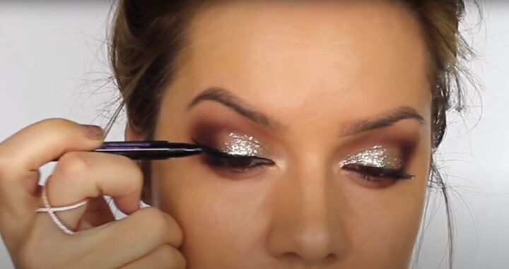 this dark sultry festive makeup look is perfect for a holiday party, Drawing winged eyeliner along the upper lid