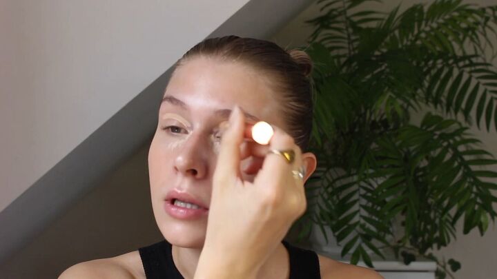 how to create a glowy bronze makeup look for spring summer, Applying concealer to eyelids