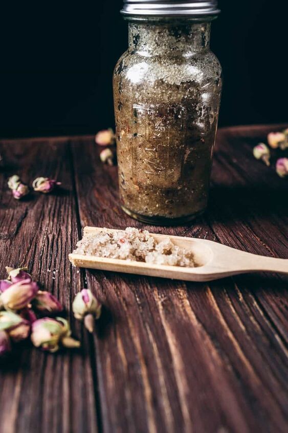 homemade diy vanilla rose sugar scrub recipe, a tall jar and wooden spoon filled with DIY sugar scrub with vanilla and rose petals