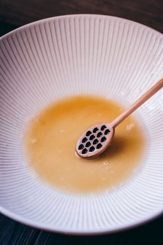 diy homemade honey bubble bath recipe, a wooden honey spoon resting in a white bowl of homemade bubble bath recipe