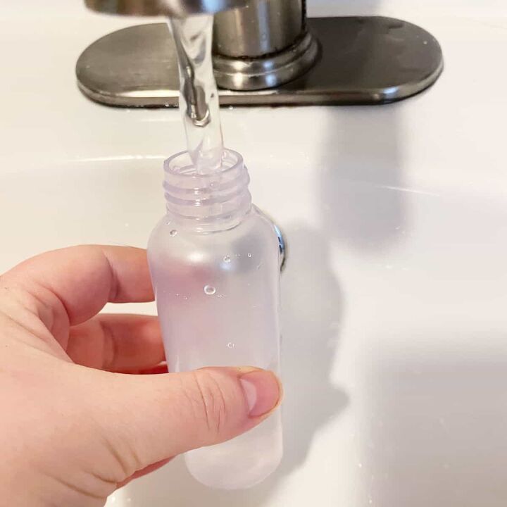 how to make your own eye makeup remover, A hand holding a small plastic bottle with water from a bathroom faucet